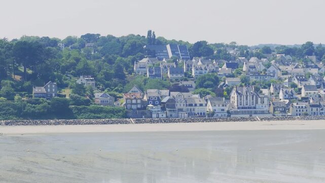 Wide panoramic footage of the coastal town of Binic in Brittany, France, showing the sandy beach at low tide with the town's traditional houses and buildings rising on the hillside.