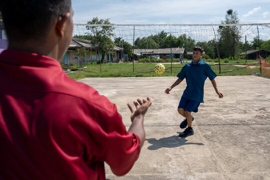 Asian man holding takraw ball preparing to serve to teammate on outdoor court. Two men standing on a concrete court preparing to start a casual game of sepak takraw on a sunny afternoon