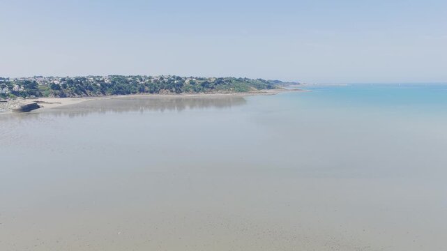 Aerial view of the sandy beach and coastal town of Binic, located in Brittany, France with a wide expanse of beach at low tide, with gentle waves, clear blue sky.