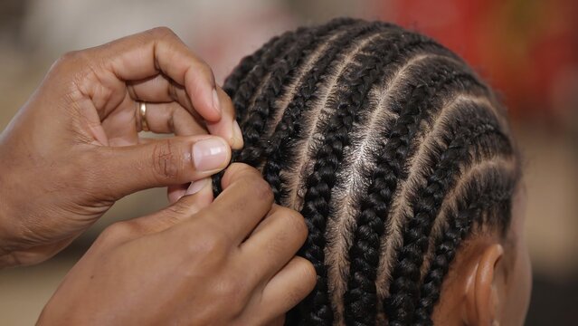 Hairdresser creates intricate braided cornrow hairstyle on woman head with precision using hands for ethnic beauty grooming service in professional hair salon studio for styling.