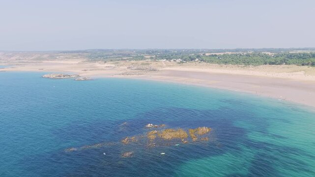 Aerial view of the sweeping coastline of Anse du Croc in Frehel, Brittany, France, turquoise waters, rocky outcrops, and an expansive sandy beach stretching along the shoreline.