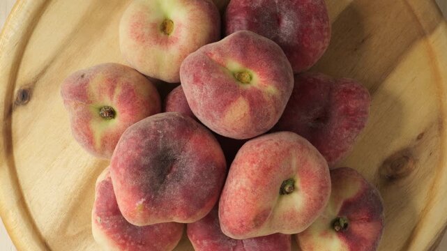 Fresh flat peaches rotating on wood board