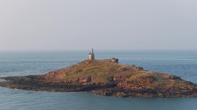 Wide shot of the Ilot Saint Michel, a small rocky island with its historic chapel, surrounded by the sea off the coast of Erquy in Brittany, France.