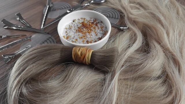 Natural human hair extensions prepared for hot fusion keratin bonding. Keratin tips, hair extension tools and clips arranged on a salon workstation, illustrating professional hair extension applicatio