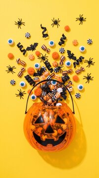 halloween candy spilling from pumpkin bucket on vibrant yellow background