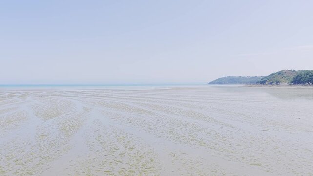 Wide static shot of Binic Beach during low tide on a clear summer day in Brittany, France.