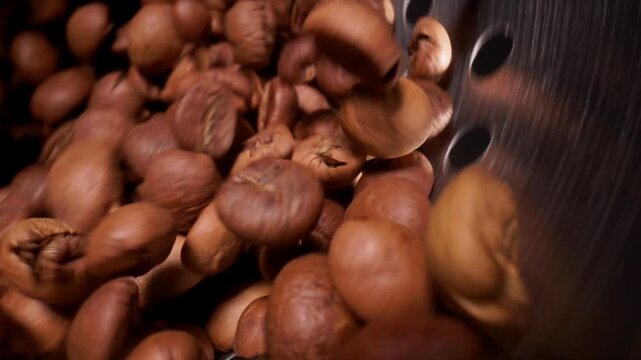 Slow motion close up of coffee beans tumbling inside metal roaster drum in warm light, food industry macro probe view.