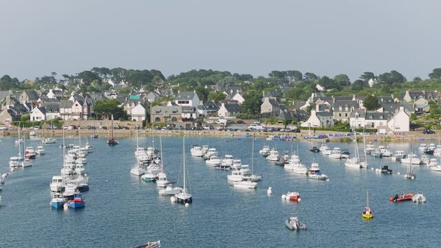 Wide daytime view of the entrance to the port of Ploumanac'h in Perros-Guirec, Brittany, France with numerous boats and yachts are moored on calm blue water.