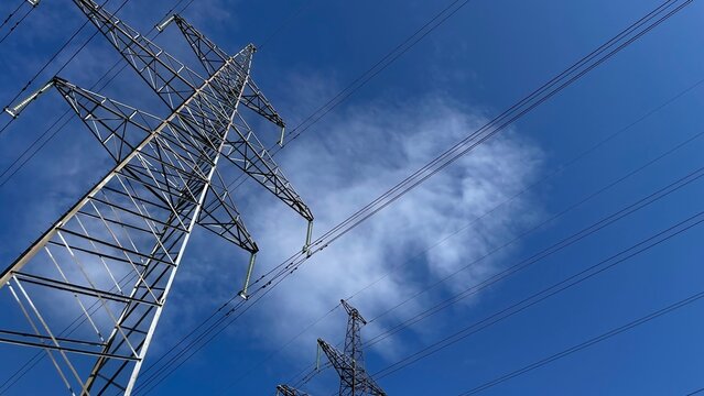 Low angle view of high voltage electricity transmission tower and power lines against vivid blue sky with soft clouds, industrial energy infrastructure and electric grid concept HD