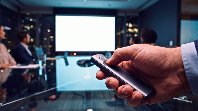 Hand holding presentation remote clicker in conference room with blank screen background for business meeting and corporate presentation