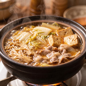 Extreme close-up of simmering nabe hot pot with steam, napa cabbage, tofu and pork in broth