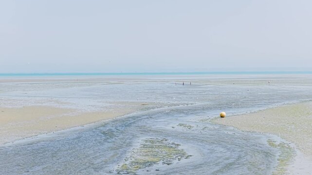 Wide shot of Binic beach in Brittany, France during low tide, revealing expansive sandy flats and shallow tidal streams.