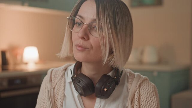 Nighttime studio music lover wearing headphones focused on laptop, warm lamp and kitchen backdrop, arranging beats and editing tracks, concentrated gaze, intimate production vibe and introspective