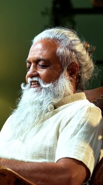 Indian mid age bearded chatting typing message using smartphone sitting on relaxing chair at home, stylish mature male engaged in mobile conversation and online communication in modern interior