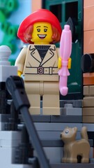 Fototapeta premium Tambov, Russian Federation - June 24, 2025 Lego woman minifigure holding an umbrella and cat standing near the entrance to a house and going down a flight of stairs. Close-up