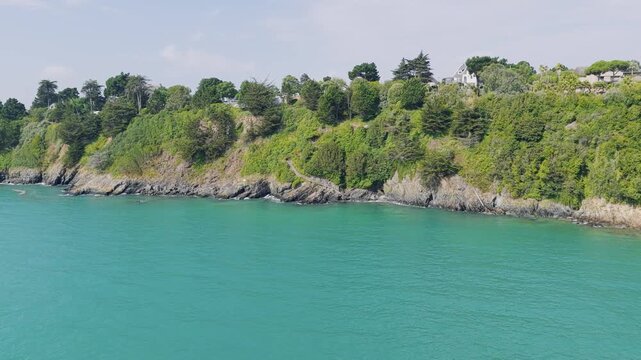 Aerial view of the dramatic green cliffs and rocky coastline of Binic, Brittany, France, lush vegetation atop rugged cliffs, with a few houses nestled among the trees.