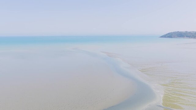 Aerial view of a wide, empty sandy beach and tidal flats with shallow water at low tide in Binic, Brittany, France.