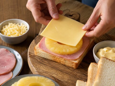 Toast Hawaii wird klassisch belegt: H&auml;nde legen K&auml;se auf Toast mit Schinken und Ananas &ndash; ber&uuml;hmter deutscher Retro-Klassiker der Nachkriegsk&uuml;che und beliebtes Ofengericht.
