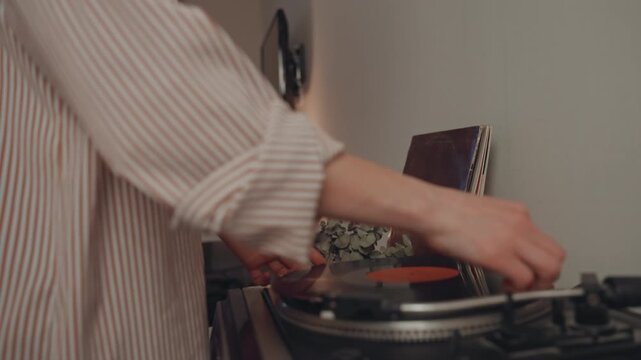Caucasian woman music lover holding vinyl, placing record on turntable with headphones around neck, cozy living room lamp light, closeup hands adjusting needle and tonearm, vintage analog warmth