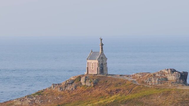 Static wide shot of the historic chapel on Ilot Saint Michel, perched atop rocky cliffs overlooking the sea near Erquy, Brittany, France.