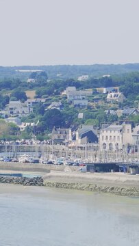 Wide view of Binic, a coastal town in Brittany, France, featuring the marina with numerous sailboats, classic French seaside architecture, and green hills in the background.