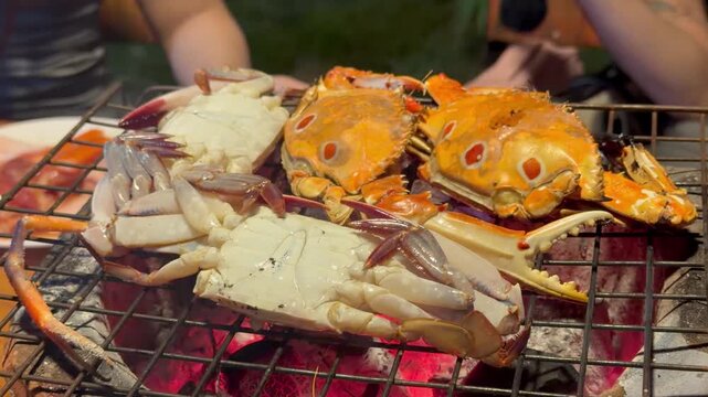 PATTAYA, THAILAND - APRIL 2026 : View of three-spot swimming crab grilling on charcoal BBQ brazier grid iron at Mookata restaurant. Local Thai food culture and dining lifestyle.