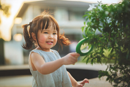 Happy toddler girl exploring green leaves with magnifying glass outdoors, curiosity and early childhood learning through nature discovery