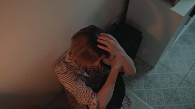 White woman curled on floor in tiled entryway hugging knees head bowed warm orange and teal glow record player on cabinet distant ambient sound music lover heartbroken introspective cinematic mood