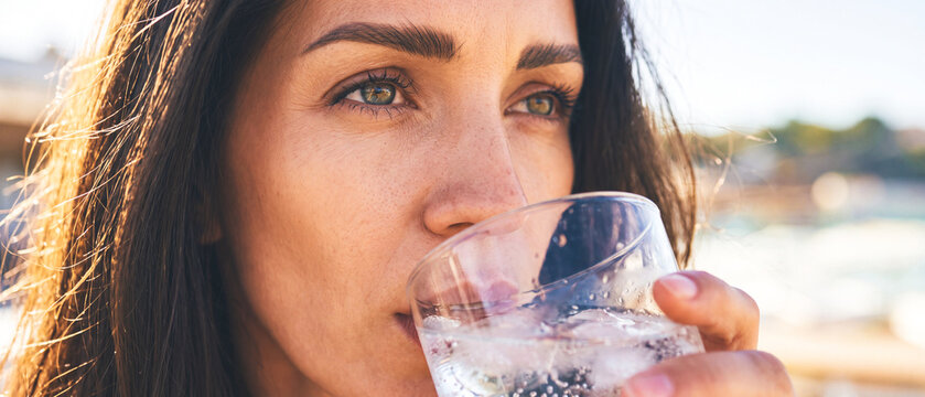 Woman sips water glass outdoors on sunny day