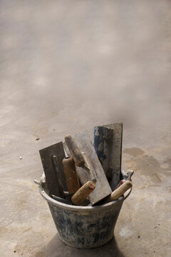 Trowel for construction tool set inside bucket for masonry plastering on concrete cement floor, equipment for builder repair work-vertical image.