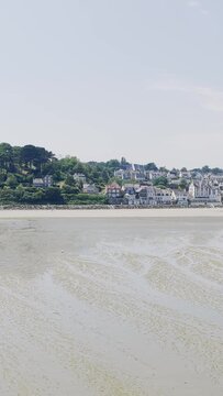 A wide, bright daytime shot of Binic beach at low tide, with wet sand stretching toward the charming seaside town.