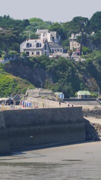 Medium telephoto shot of elegant houses perched on a green clifftop overlooking the port of Binic in Brittany, France.