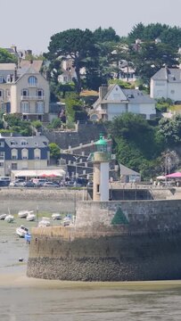 Static shot of a small lighthouse with a green top standing on a stone harbor wall at low tide in Binic Port, Brittany, France.
