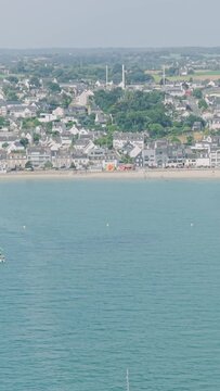 Aerial view of the seaside town of Binic in Brittany, France, showing the waterfront, sandy beach, harbor, and surrounding residential area on a clear summer day.