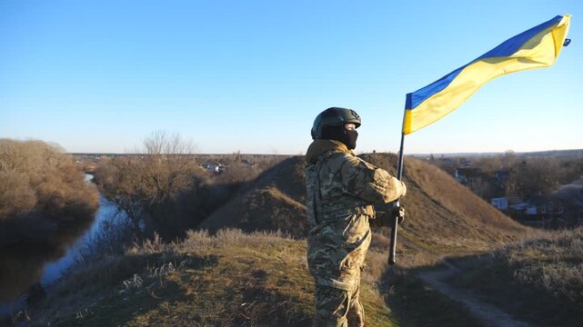 Female military in uniform waving flag of Ukraine at countryside. Young soldier of ukrainian army lifting national banner as symbol of victory against russian aggression. Invasion resistance concept