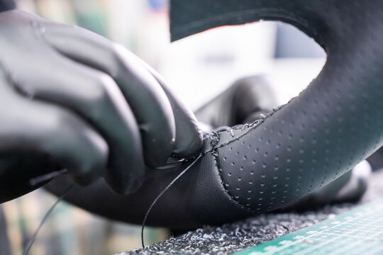 A seamstress in a workshop makes a new leather cover for a car steering wheel.