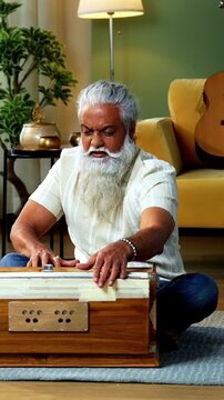 Indian mid age stylish bearded man practicing vocals or singing at home, dedicated to daily riyaz while accompanying harmonium in modern home studio interior setting