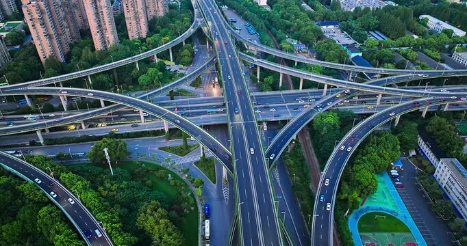 Multilevel highway interchange crossing a green urban district in Nanjing, China, showing dense traffic, elevated ramps, apartment towers, and a basketball court.
