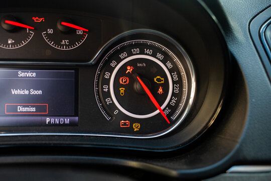 Illuminated warning lights and a service display appear on a modern car dashboard cluster. The visual highlights vehicle diagnostic alerts requiring professional auto repair and routine maintenance.