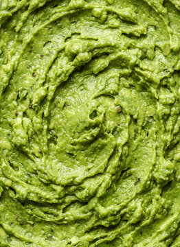 Close-up macro view of freshly mashed avocado or creamy guacamole. Full frame food texture background featuring vibrant green swirls, chunks, and smooth paste. Concept for healthy vegan eating, Mexica