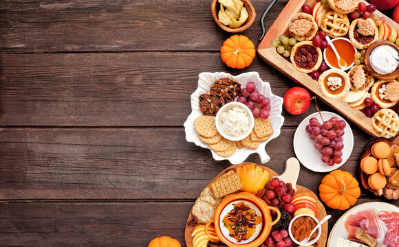 Autumn or Thanksgiving appetizers, sweets and grazing boards. Overhead view side border on a dark wood background. Pumpkin and apple snacks, charcuterie, pies, desserts.
