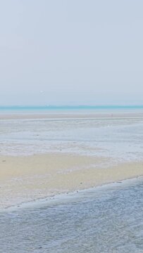 A wide sandy beach in Binic, Brittany, France, is captured at low tide on a clear summer day.