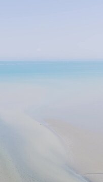 Aerial view of an empty sandy beach meeting calm, clear blue sea under a bright sky at Binic, Brittany, France.