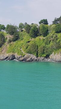Aerial view of the lush green cliffs and rocky shoreline meeting the vibrant turquoise waters in Binic, Brittany, France.