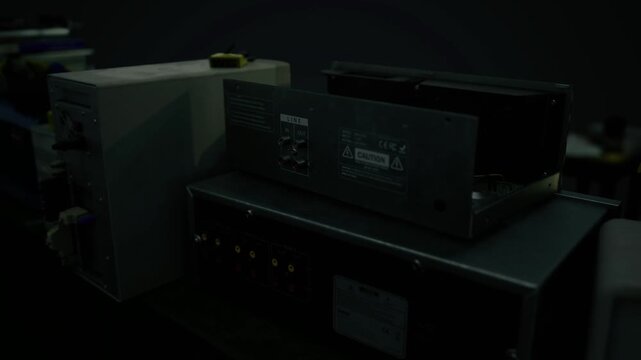 Rack of amplifiers and modules with cabling and knobs in low light, stacked units and ventilation grills visible, studio or stage gear undergoing tuning