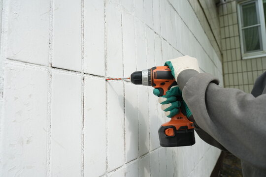 Drilling tiled exterior wall with orange cordless drill
