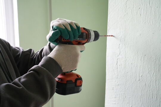 Man drilling concrete wall with cordless screwdriver close-up