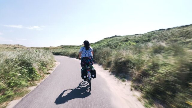 Cyclist riding toward the sea on a Dutch coastal path
