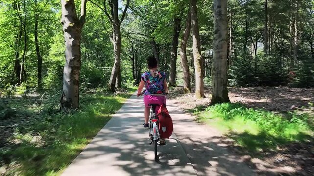 Woman cycling through a green woodland in summer
