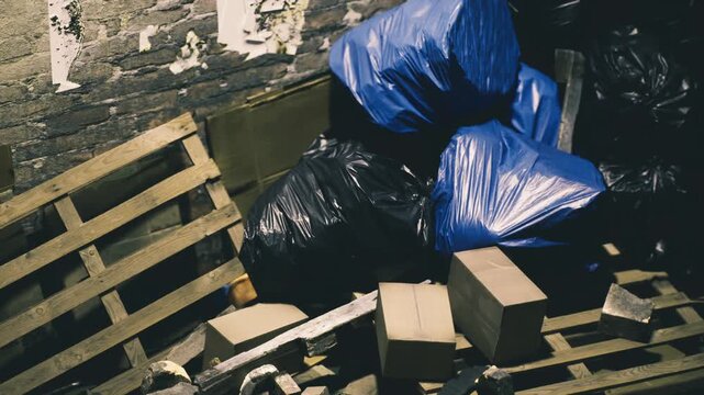 Amidst the dim light of an abandoned space, scattered debris, wooden pallets, and blue garbage bags create a chaotic scene of urban neglect, rich with stories waiting to be uncovered.